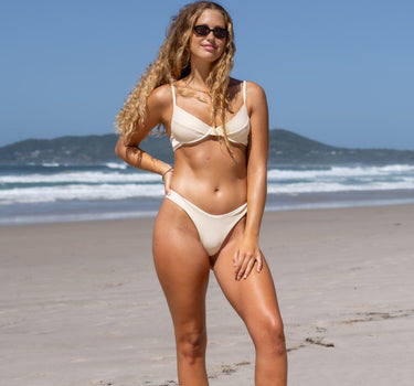 Model showcases the versatility of F.lux's cream Amy Ribbed Bikini Bottoms, perfectly paired for a chic, eco-conscious poolside look, highlighting the brand's commitment to luxury and sustainability.